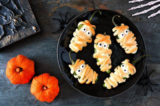Halloween mummy jalapeno poppers, top view with decor on a dark stone background - Photo, Image
