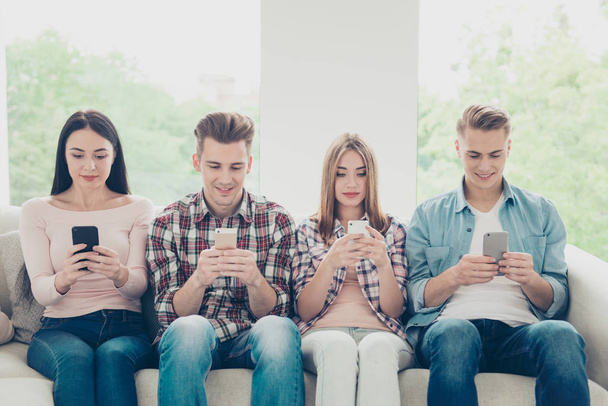 Four young people in jeans and shirts holding modern phones and  - Foto, imagen