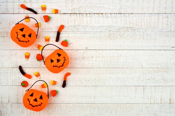 Halloween side border with Jack o Lantern pails and spilling candy. Above view on a white wood background. Copy space. - 写真・画像