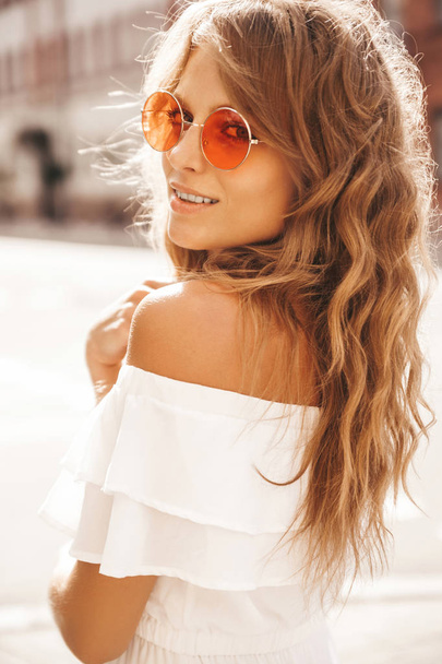 Portrait of beautiful cute blond teenager model with no makeup in summer hipster white dress clothes posing on the street background in sunglasses - Foto, afbeelding
