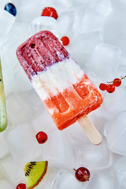 Creamy fruit colored ice cream lolly with different berries and slices of watermelon on ice cubes. Summer dietary cold dessert. Flat lay - Photo, Image