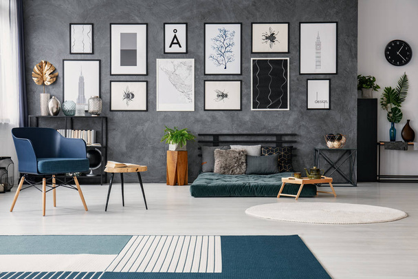 Carpet in grey spacious flat interior with blue armchair next to table near green futon. Real photo - Photo, Image