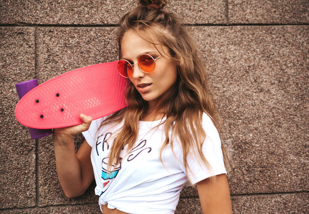 Beautiful cute blond teenager model without makeup in summer hipster white clothes with pink penny skateboard posing near wall on the street - Fotografie, Obrázek