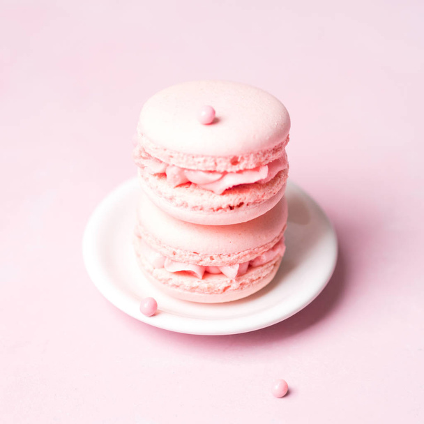 Stack of french strawberry macaroons on saucer over pink pastel background - Foto, afbeelding