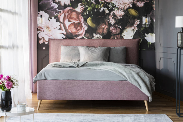 Grey sheets on pink bed in feminine bedroom interior with flowers print on the wall. Real photo - 写真・画像