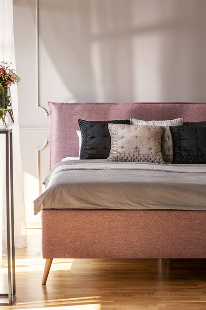 Pillows on bed in grey and pink bedroom interior with flowers and wall with molding. Real photo - Photo, Image