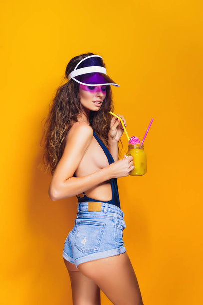 Sexy Woman in white swimsuit and blue jeans shorts, trendy visor holding beverage - Photo, Image