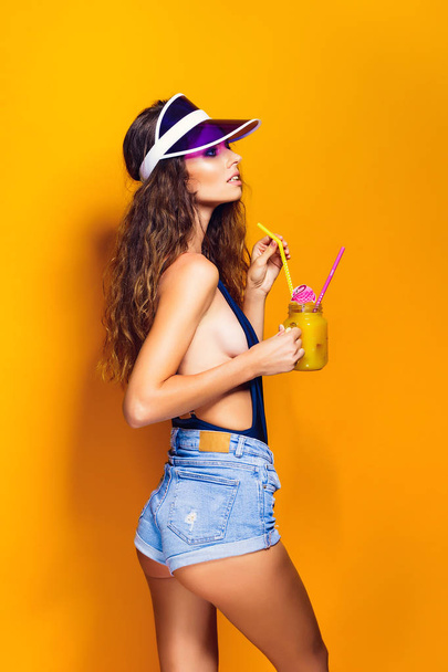 Sexy Woman in white swimsuit and blue jeans shorts, trendy visor holding beverage - Photo, image