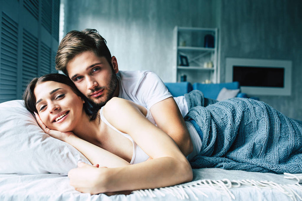 Young heterosexual couple cuddling on bed - 写真・画像