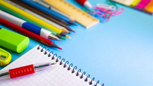 School levert op blauwe achtergrond. Pennen, potloden, liniaal, paperclips, laptop voor copyspace en markering op de tafel. Bekijk van bovenaf met kopie ruimte - Foto, afbeelding
