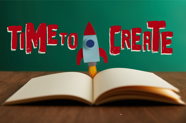 open book with colorful rocket on wooden table with "time to create" lettering   - Photo, image