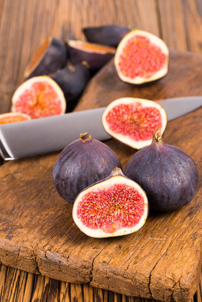Group of whole and sliced ripe, delicious and sweets figs with a kitchen knife on a old rustic wooden cutting board - Foto, Imagen