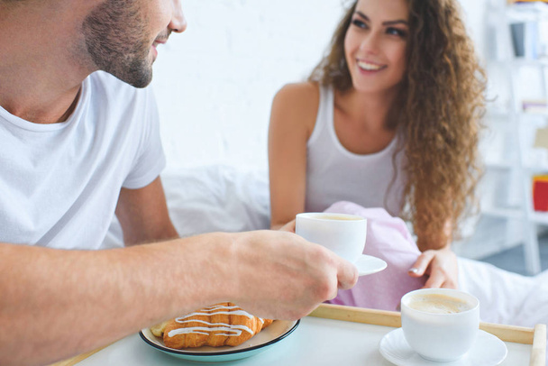 cropped shot of smiling young couple having croissants and coffee for breakfast in bed   - 写真・画像