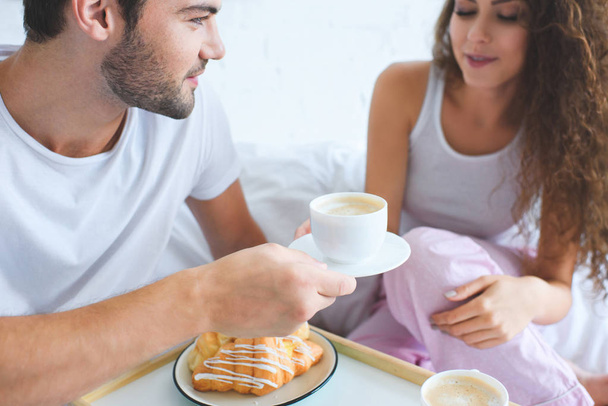 plan recadré de jeune couple ayant croissants et café pour le petit déjeuner au lit
  - Photo, image