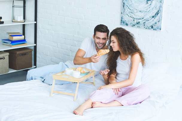 высокий угол зрения счастливой молодой пары в пижаме, завтракающей вместе в спальне
 - Фото, изображение