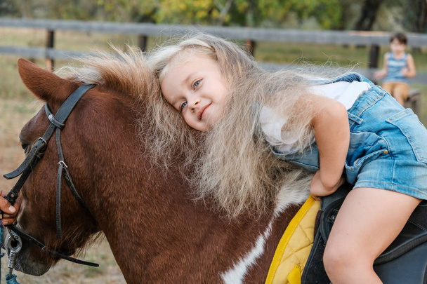 A cute little blonde girl is sitting on a pony in autumn. - Photo, Image