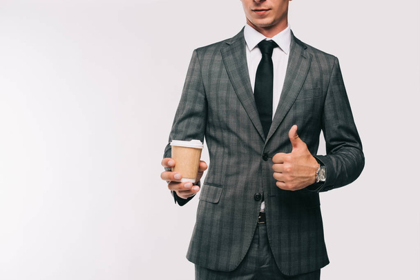 levágott kép üzletember gazdaság kávé papírpohár, és bemutatja a hüvelykujjával felfelé a elszigetelt fehér - Fotó, kép