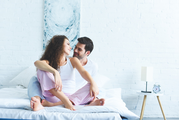 heureux jeune couple en pyjama assis sur le lit et se souriant
 - Photo, image