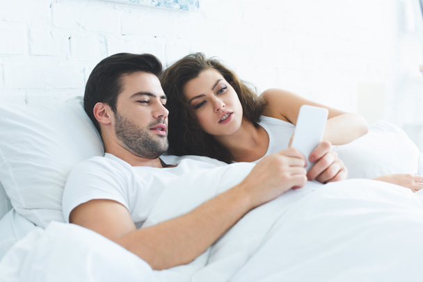 young couple lying in bed and using smartphone together - Φωτογραφία, εικόνα