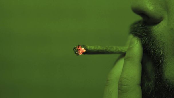 um jovem fumando um jointer rolou com botões de erva dentro na luz verde close-up
. - Foto, Imagem