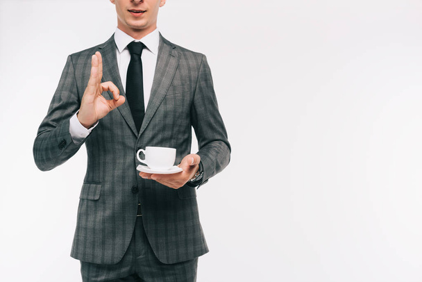 abgeschnittenes Bild eines Geschäftsmannes, der eine Tasse Tee in der Hand hält und eine auf Weiß isolierte Geste zeigt - Foto, Bild