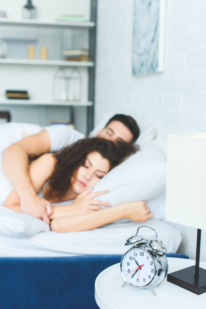 close-up view of alarm clock and young couple sleeping in bed behind  - Foto, afbeelding