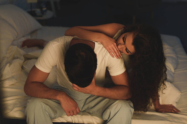 jonge vrouw kijkt boos vriendje zittend op bed's nachts, relatie problemen concept  - Foto, afbeelding