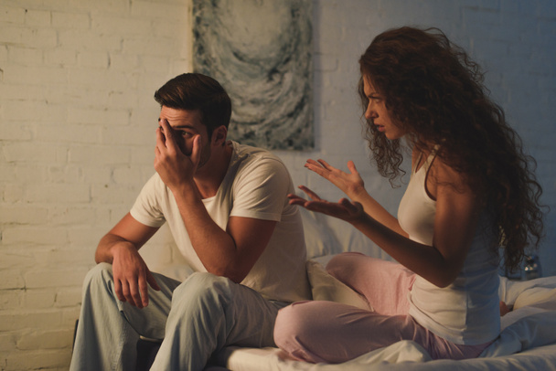 Emotionale junge Frau streitet mit aufgebrachtem Freund im Bett, Beziehungsschwierigkeiten - Foto, Bild