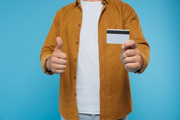 abgeschnittenes Bild eines Mannes, der den Daumen nach oben zeigt und Kreditkarte isoliert auf blauem Grund hält - Foto, Bild