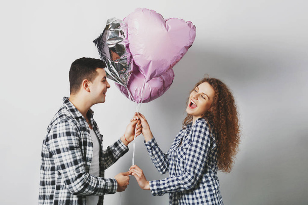 Cute joyful curly woman happy to recieve heart balloons from boyfriend who is very romantic, pose together against white background, have satisfied expressions, People, date and relationship - Photo, Image