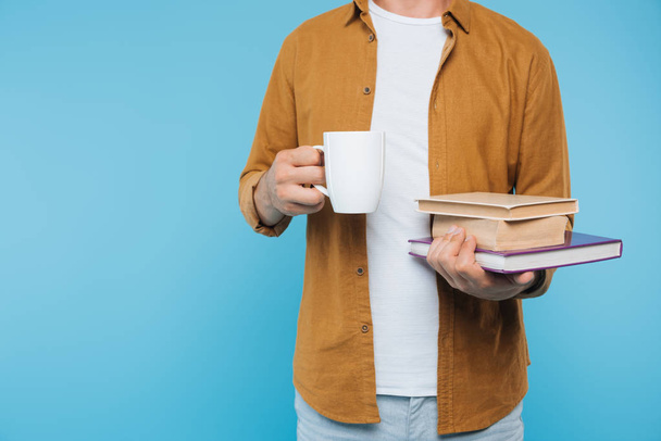 abgeschnittenes Bild eines Mannes mit Büchern und einer Tasse Tee isoliert auf blauem Grund  - Foto, Bild