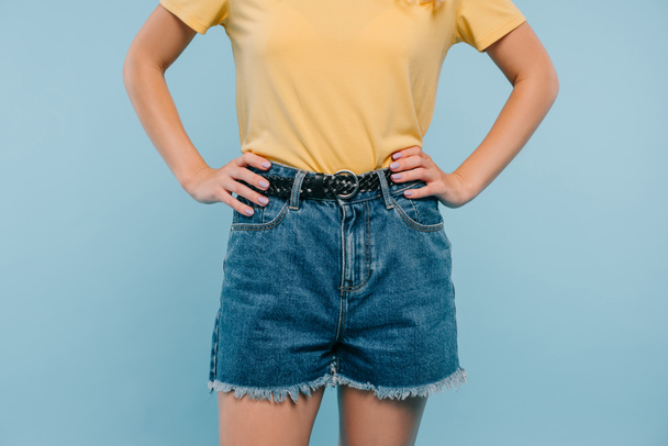 обрезанный образ девушки в рубашке и шортах стоя с руками акимбо изолированы на синий
 - Фото, изображение