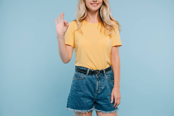cropped image of girl in shirt and shorts showing okay gesture isolated on blue - Valokuva, kuva