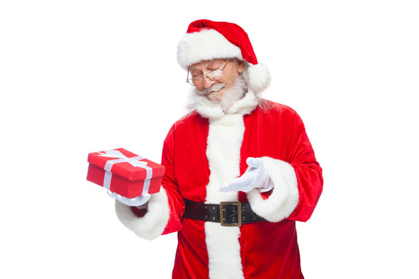 Christmas. Smiling Santa Claus in white gloves is holding a gift red box with a bow. Pointing at the gift. Isolated on white background. - Foto, Bild
