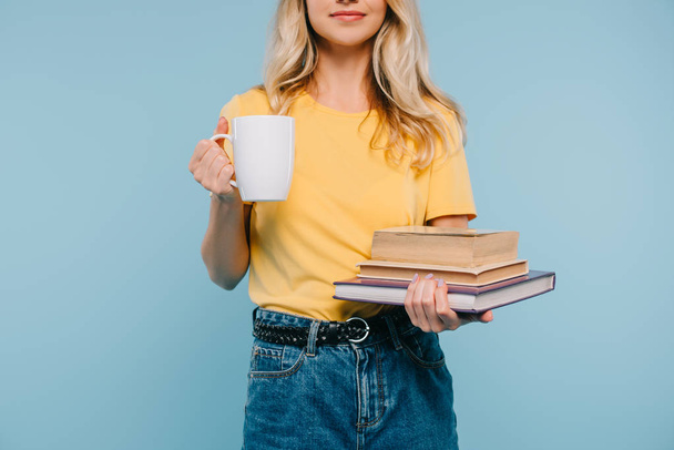 bijgesneden afbeelding van meisje houdt van boeken en kopje koffie geïsoleerd op blauw - Foto, afbeelding