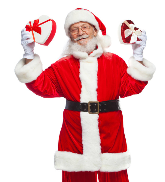Vánoce. Usmívající se Santa Claus v bílých rukavicích drží dva dárkové krabičky ve tvaru srdce červené a bílé se stuhou. Koncept štědré dary. Izolované na bílém pozadí. - Fotografie, Obrázek