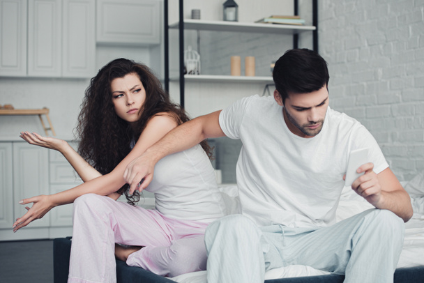 Unzufriedenes junges Paar streitet, während Mann Smartphone nutzt, Konzept für Beziehungsprobleme  - Foto, Bild