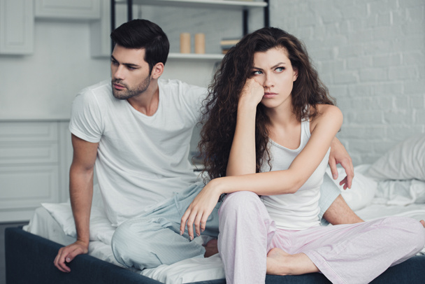 δυσαρεστημένοι από νεαρό ζευγάρι στο πιτζάμες έχοντας διαμάχη στο κρεβάτι, σχέση δυσκολίες έννοια - Φωτογραφία, εικόνα