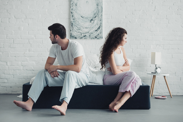 bouleversé jeune couple en pyjama assis avec les bras croisés sur le lit, concept de difficultés relationnelles
 - Photo, image