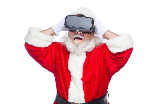 Christmas. Santa Claus in black virtual reality glasses makes gestures with his hands. Surprise, emotion. New technology. Isolated on white background. - Zdjęcie, obraz