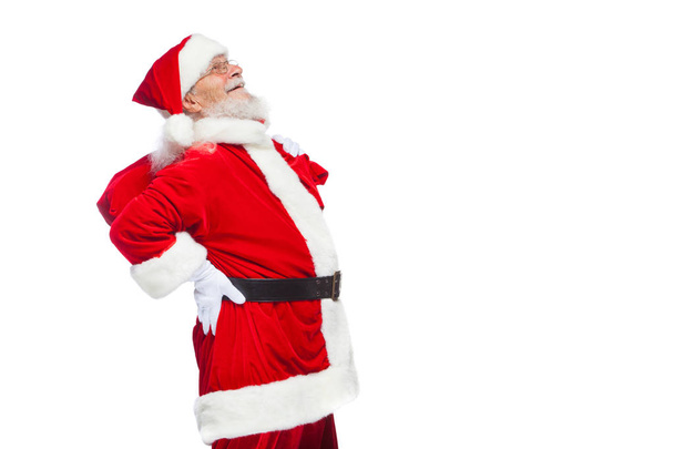 Kerstmis. Santa Claus rugpijn lijdt en houdt een rode tas met geschenken op zijn rug. Geïsoleerd op witte achtergrond. - Foto, afbeelding