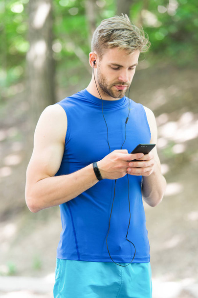 Man athlete on busy face set up play list, nature background. Sportsman training pedometer and headphones gadgets. Athlete with bristle with fitness tracker or pedometer. Gadget make life easier - Fotografie, Obrázek
