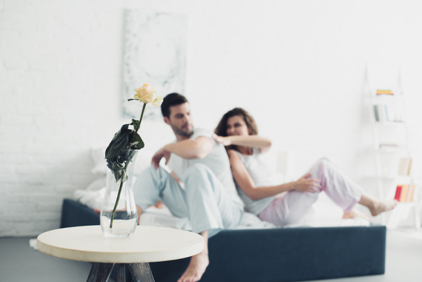 rose flower in vase and young couple quarreling on bed behind - Foto, afbeelding