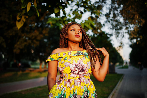 Cute small height african american girl with dreadlocks, wear at coloured yellow dress, posed at sunset. - Foto, imagen
