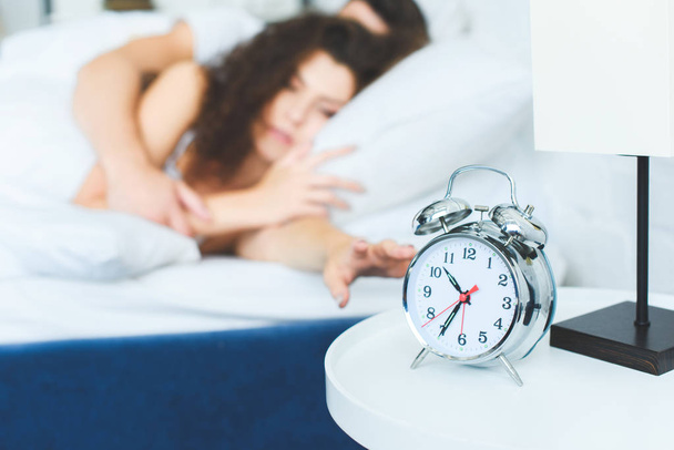 close-up view of alarm clock and young couple waking up in bed - Fotoğraf, Görsel