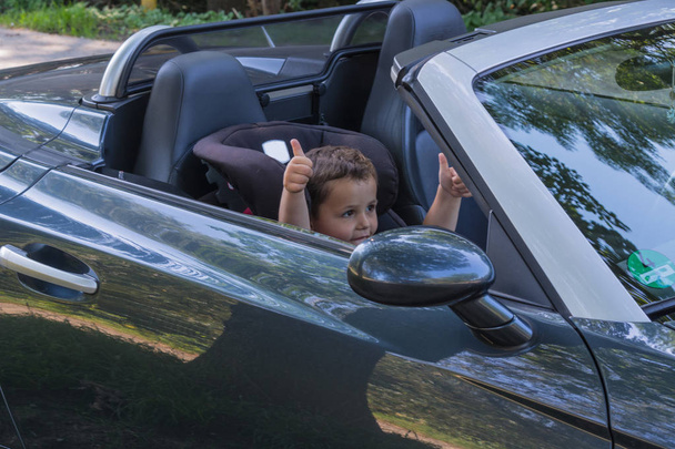 Joyeux enfant riant dans une décapotable assis dans le siège enfant de la voiture et montre les pouces vers le haut
. - Photo, image