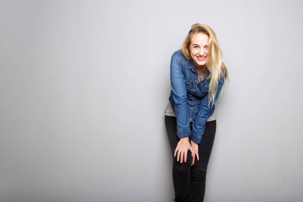 Портрет счастливой молодой блондинки, опирающейся на колено на сером фоне
 - Фото, изображение