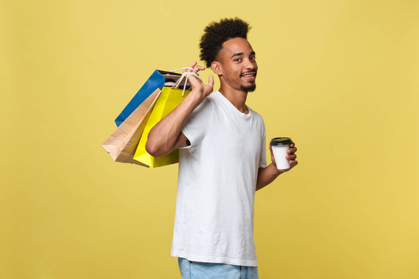 Homem afro-americano com sacos de papel coloridos isolados em fundo amarelo
 - Foto, Imagem