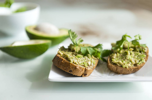 sandwiches with bread and avocado, a sprig of parsley, on a plate, useful tasty food - Foto, afbeelding