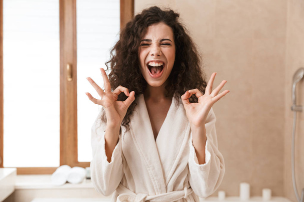 Image of excited beautiful young cute woman looking camera in bathroom showing okay gesture. - Foto, imagen